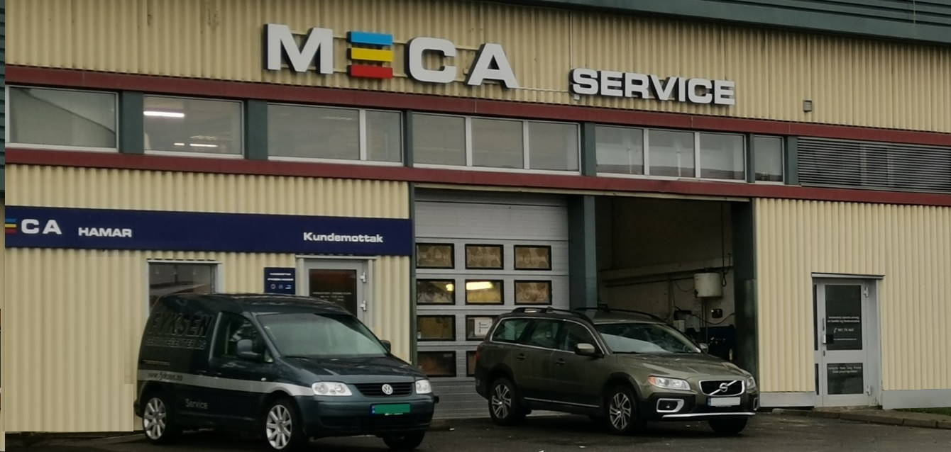 Beige verkstedbygg med MECA service skilt på veggen og to parkerte biler utenfor