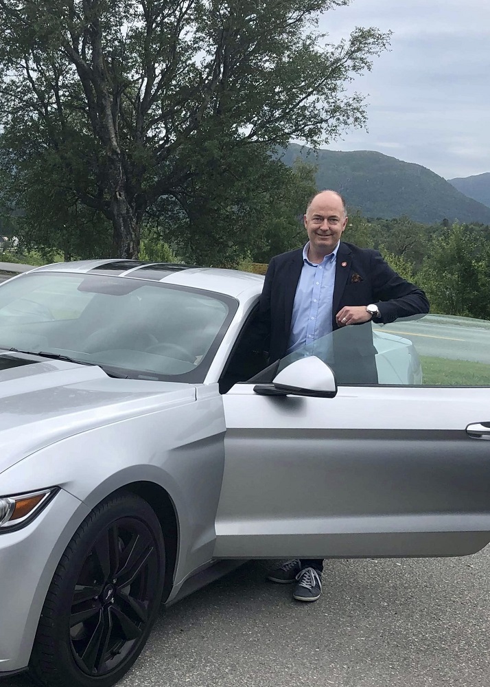 Morten Stordalen, bilpolitiske talsmann i FrP stpr i døren på sin sølvgrå Ford Mustang