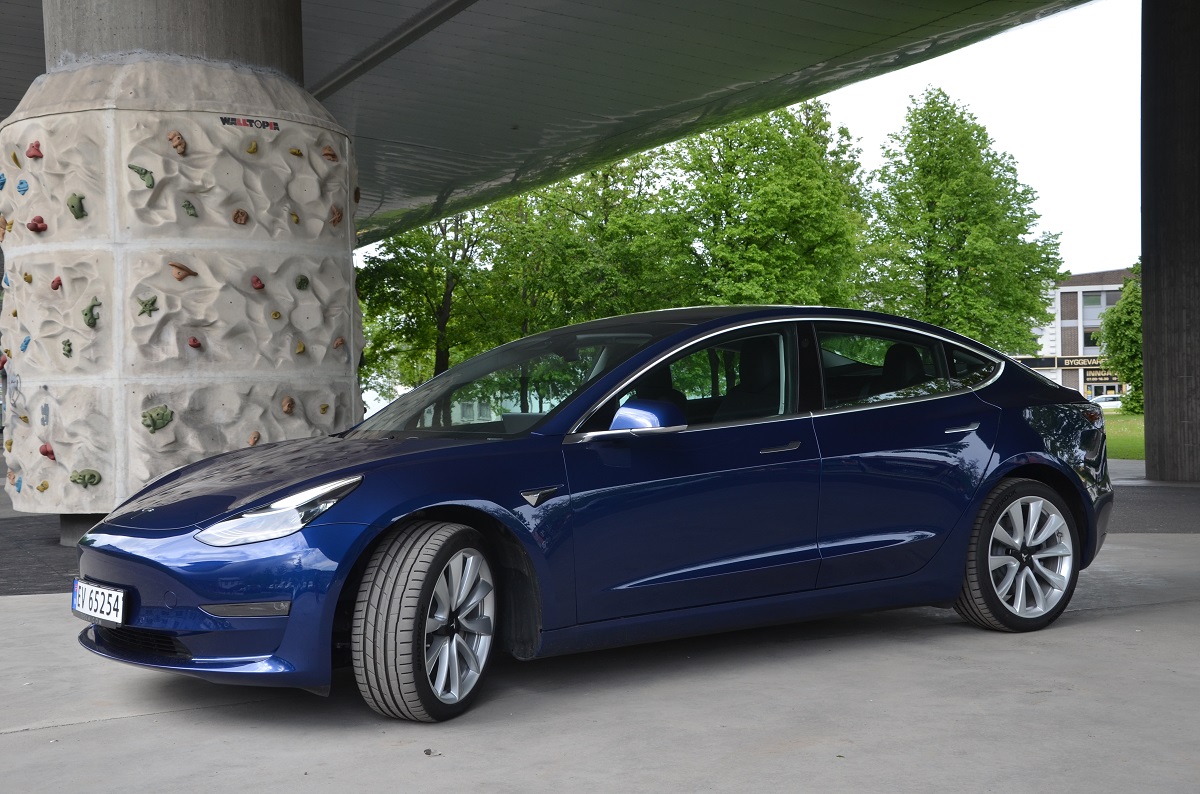 Blå Tesla Model 3 parkert under bro