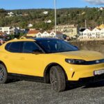 Gul Ford Capri parkert foran bebyggelse en sommer dag