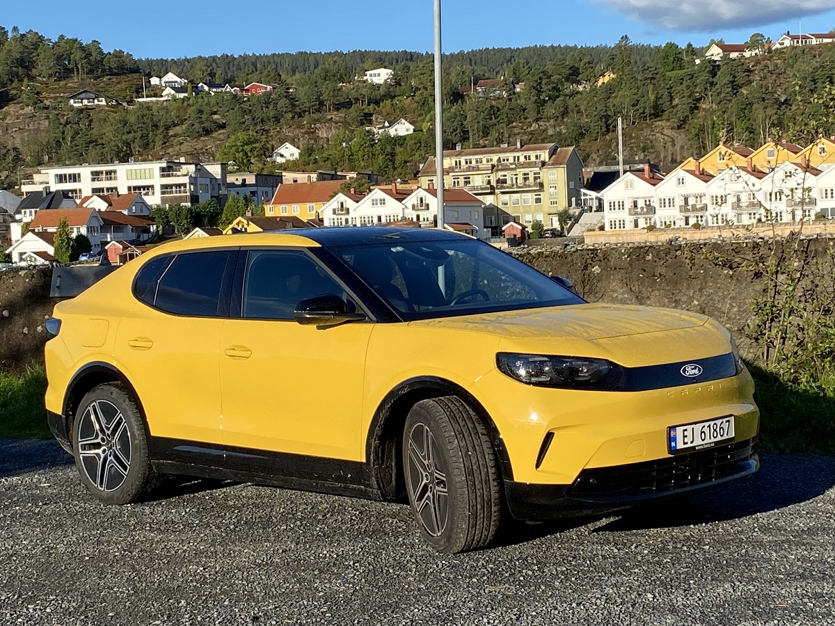 Gul Ford Capri parkert foran bebyggelse en sommer dag