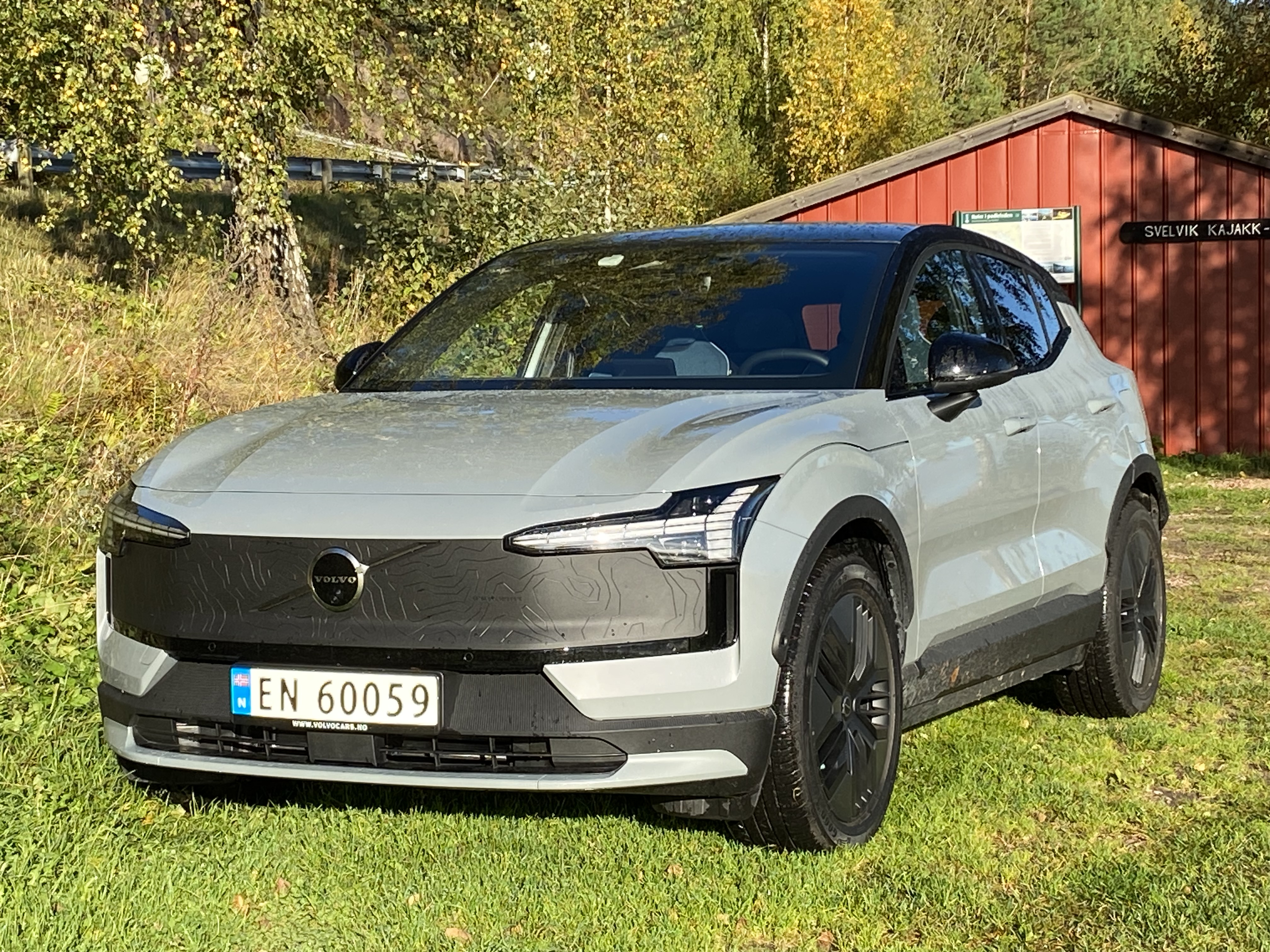 Grå Volvo er EX30 parkert på en grønn plen foran ett rødt hus