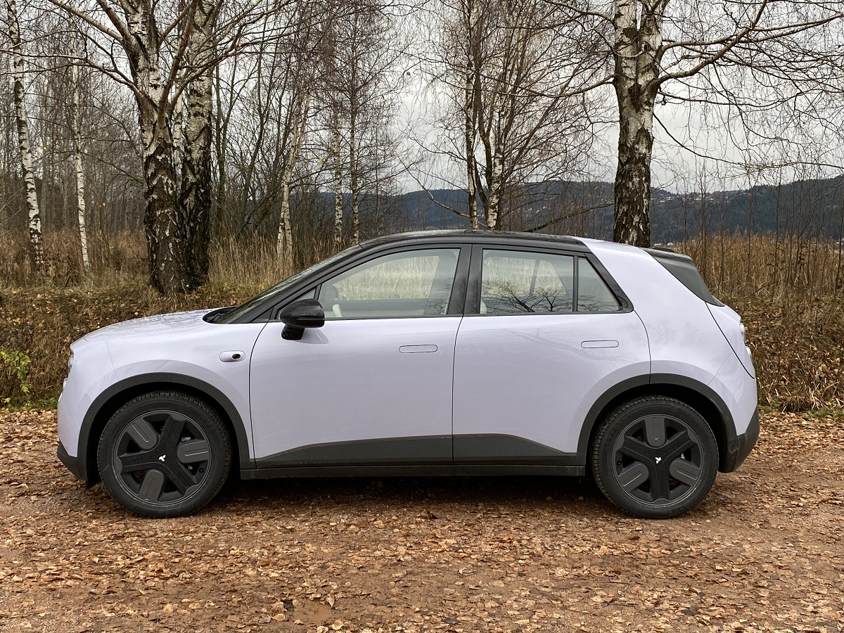 Hvit Firefly fra Nio parkert i skogen med høstløv på bakken