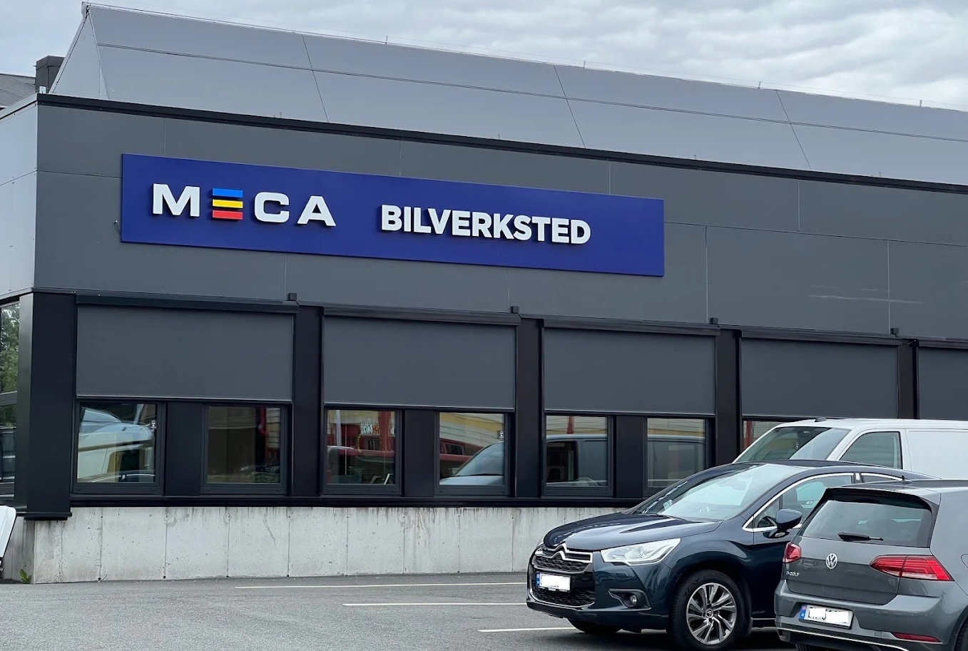 Utvendig grått, moderne verkstedbygg med MECA Bilverksted skilt på veggen